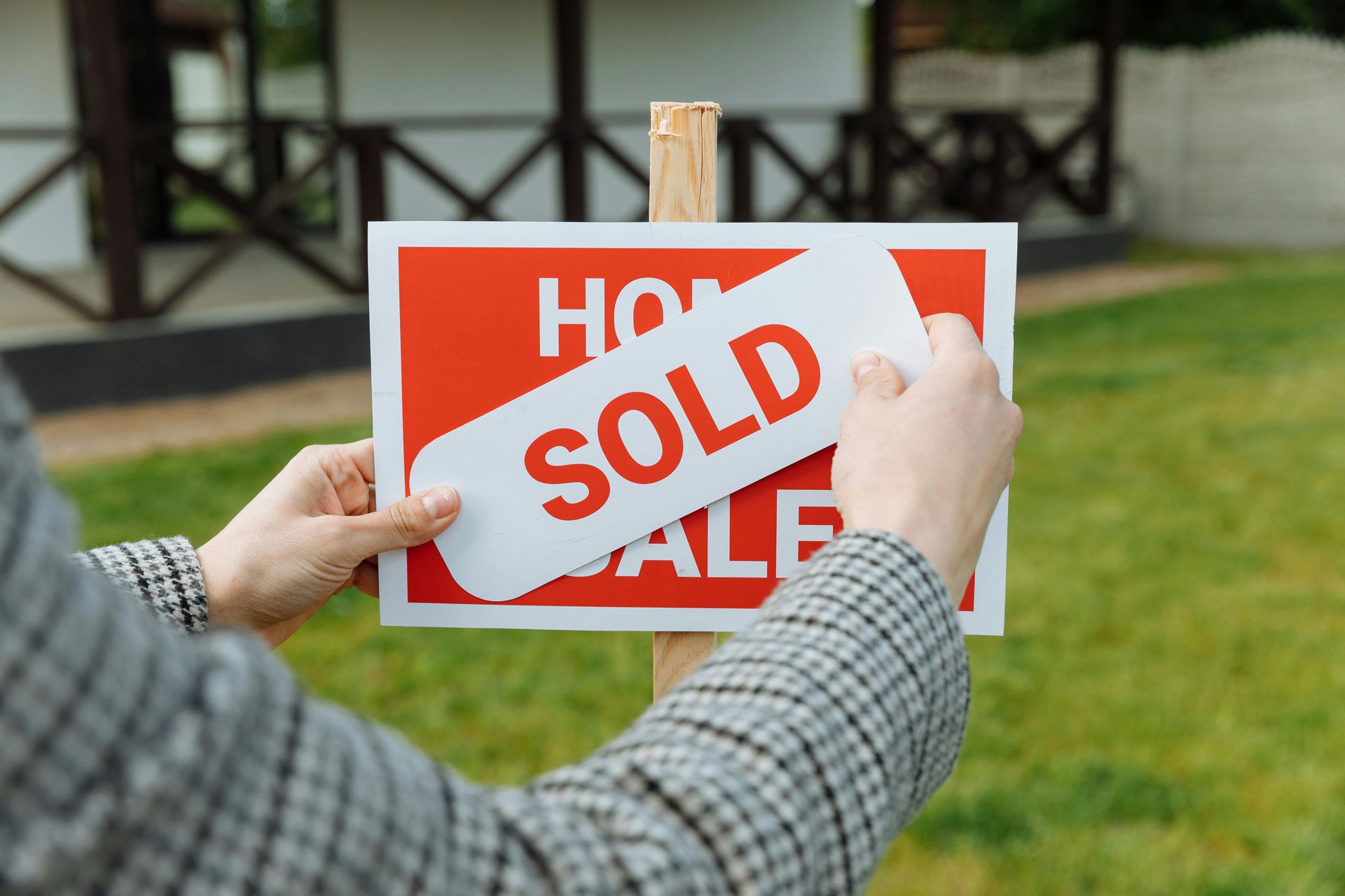 Person placing a “Sold” sign over a home‑for‑sale sign.