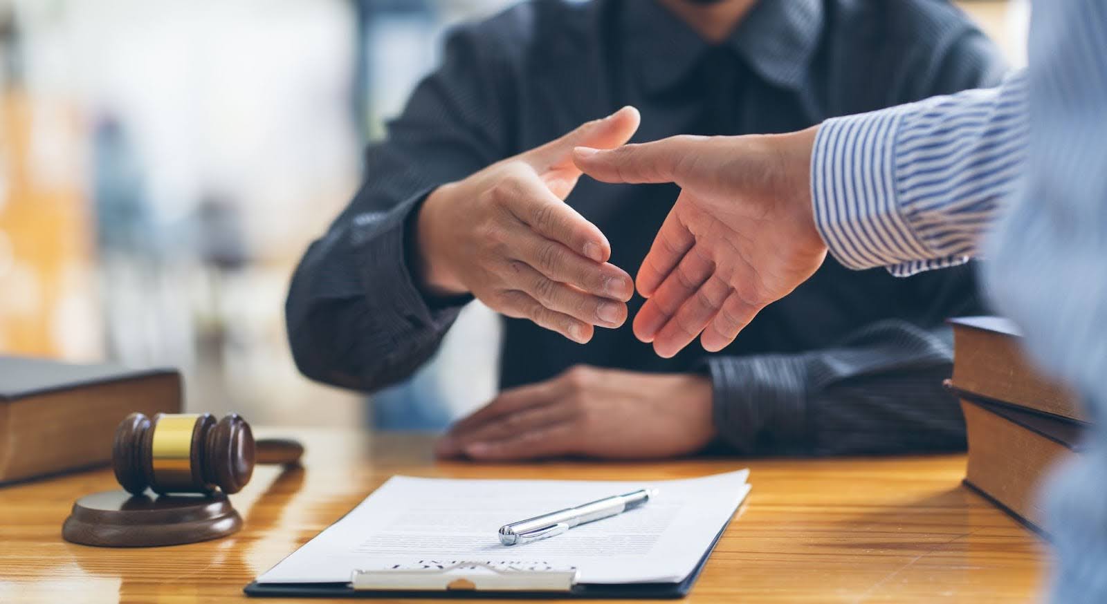 Two people shaking hands over a desk with legal documents and a gavel.